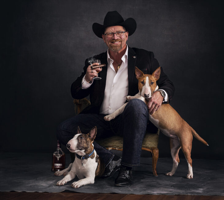 Portrait of man with two dogs smoking and drinking fine bourbon